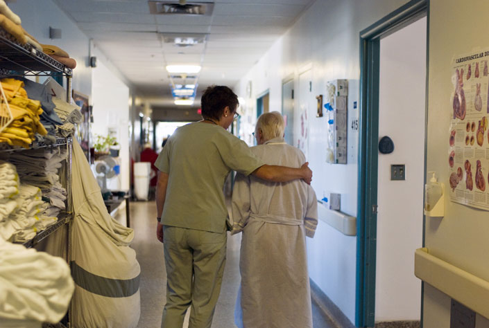 Nurse and elderly woman walking down hospital hallway together